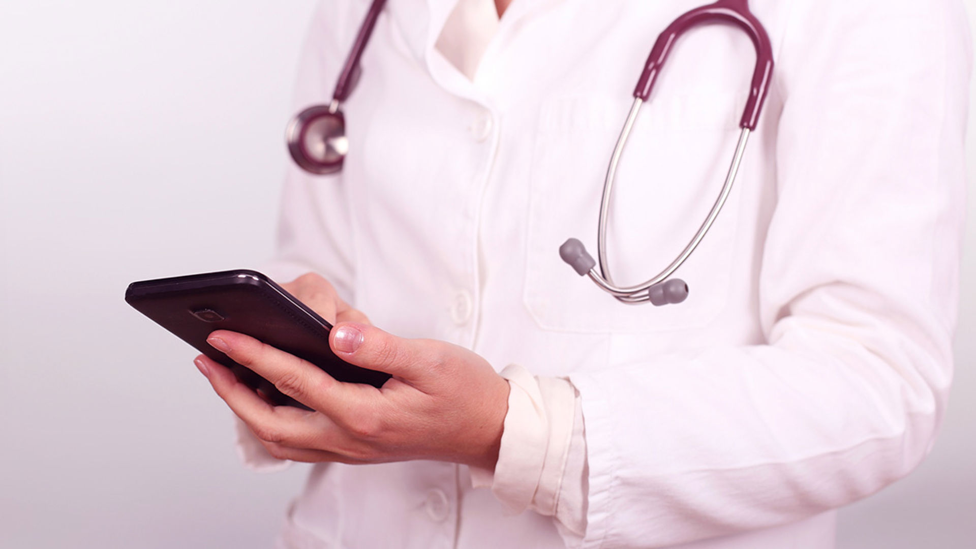 Vårdpersonal med stetoskop kollar i telefonen